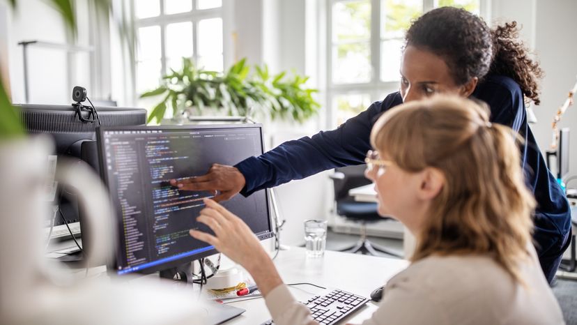 A business woman discussing with a colleague over a computer code.