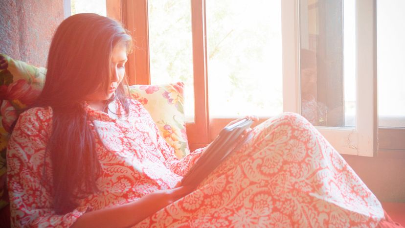 A woman using a tablet while sitting beside a window. 
