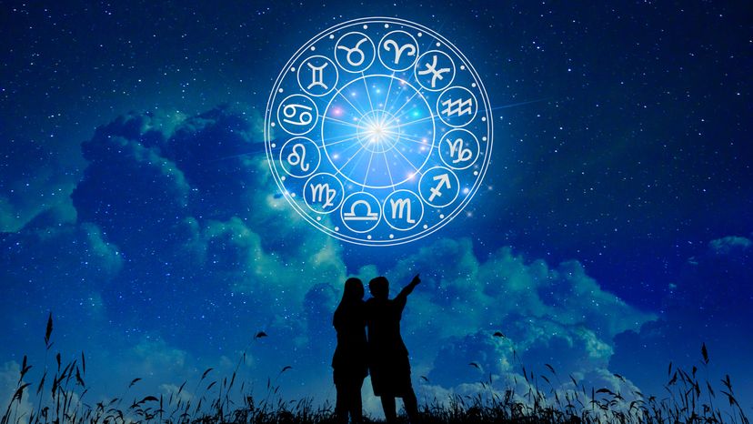 A couple standing in front of zodiac signs inside a horoscope circle in the sky. 