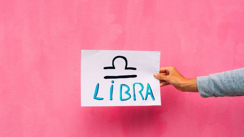 Libra sign drawn on white paper against a pink background. 