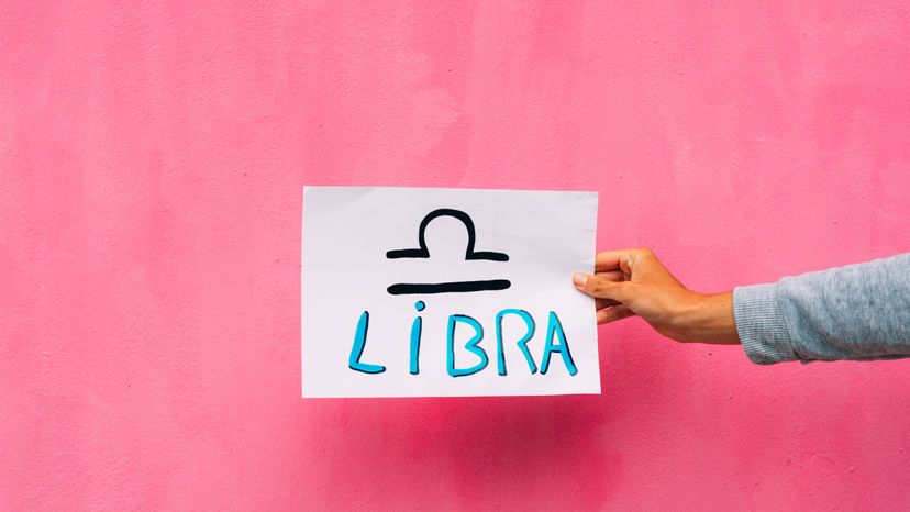 Libra sign drawn on white paper against a pink background.