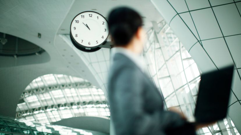 A business woman holding her laptop while looking at a clock