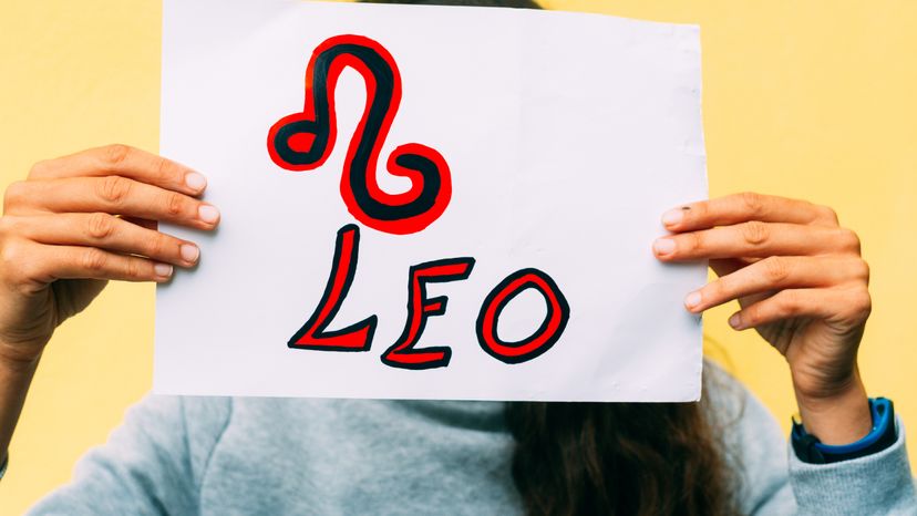 A young woman holding a Leo sign drawn on paper. 