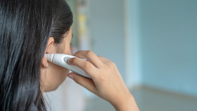 A rear view of a young girl using an ear thermometer on her right ear. 