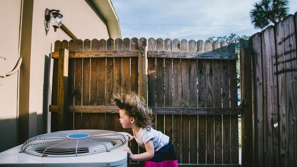 little girl standing over AC fan outside