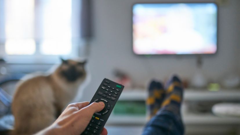 A man sitting on a couch while watching television in a living room. 