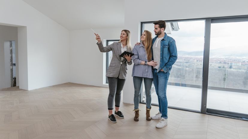 A young couple in an empty apartment talking to a real estate agent. 