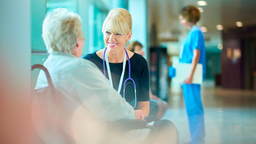 An elderly woman sits in a wheelchair talking to her doctor. 