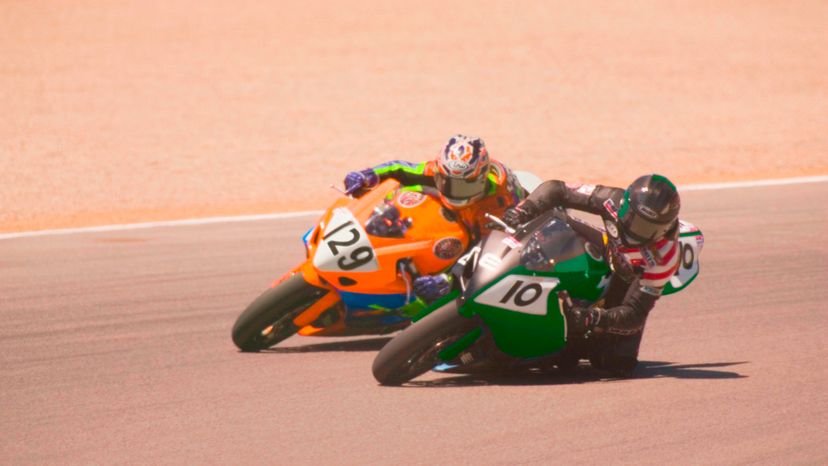 Two motorcycle racers, racing in sand. 