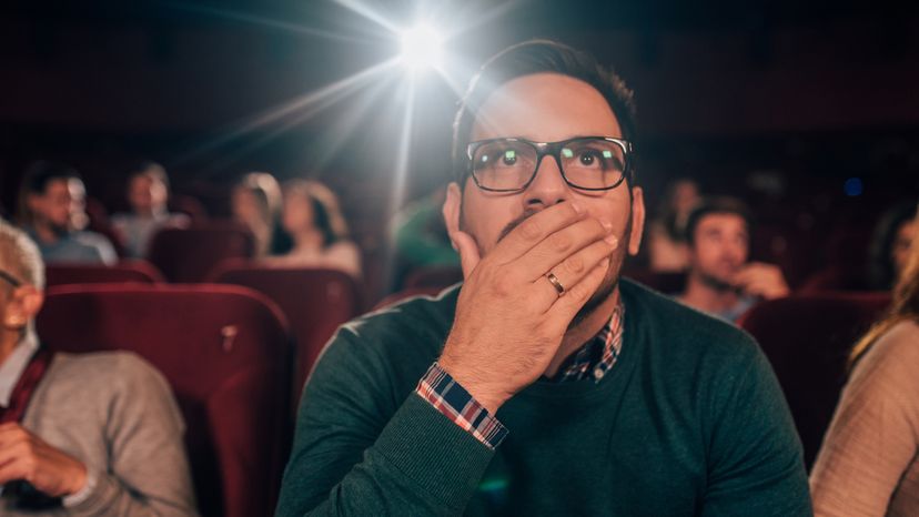 A young man in a cinema with a shocked expression on his face.