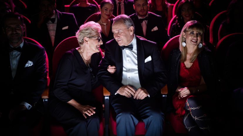 An elderly couple talking while sitting in a theater. 