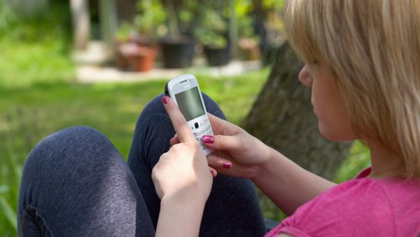 A teenage girl using a blackberry phone while siting on a lawn.