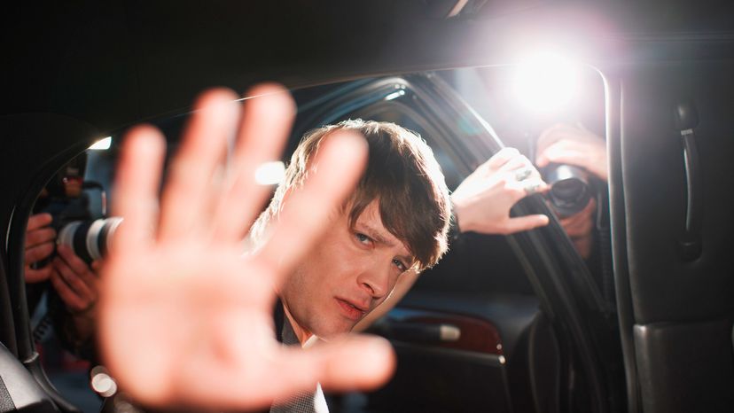 A celebrity using his hand to shield his face away from the flashes of cameras. 