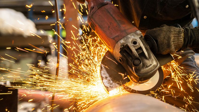 A metal worker cutting a metal object with a circular saw. 