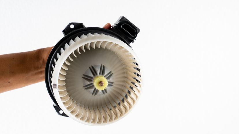 A hand holding a car air conditioner blower motor against a white background. 