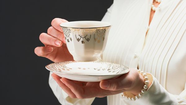 A woman holding a teacup and saucer made with china patterns. 