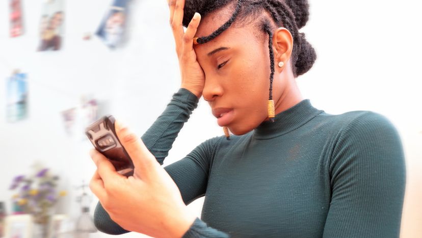 A mixed race woman holding a phone while looking frustrated. 