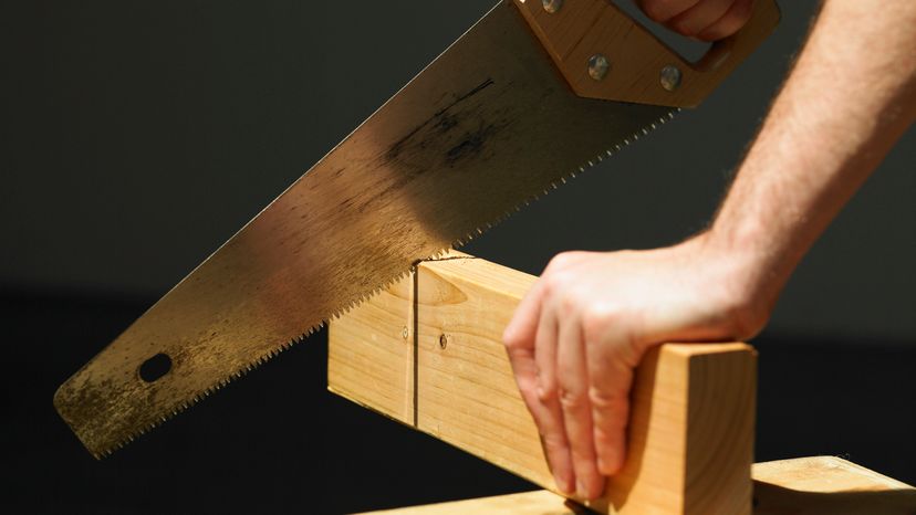 A man using a saw to cut through a wooden plank. 