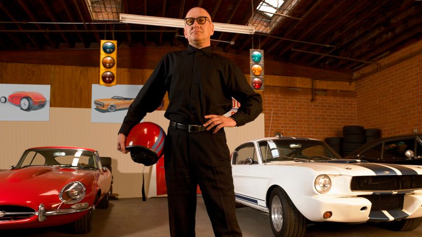 A man standing in front of two classic cars. 