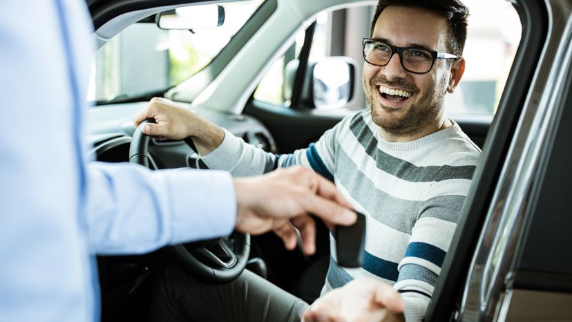 A smiling man receiving the keys to his new car. 