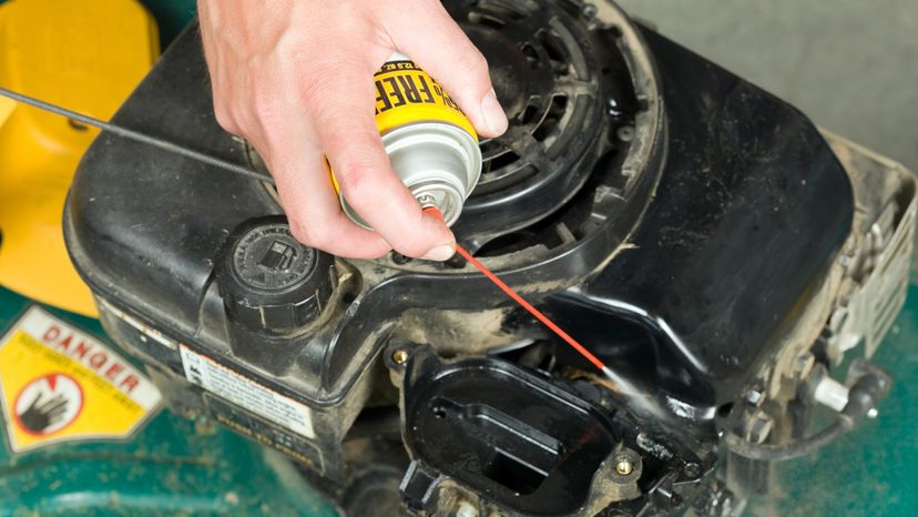 A male hand using a spray cleaner on a carburetor. 