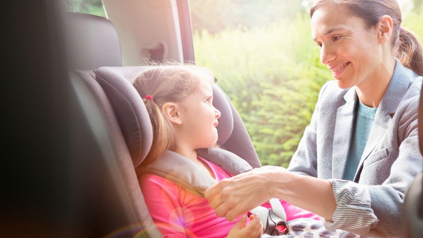 A woman placing her daughter in a car seat. 