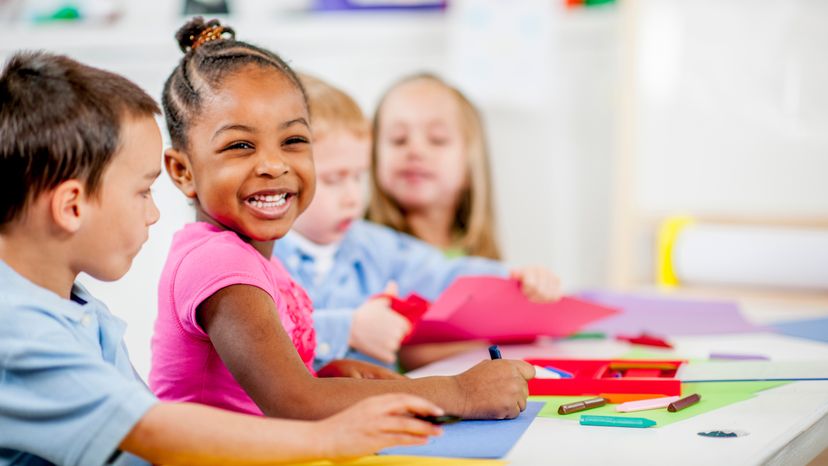 A group of children laughing while drawing with crayons. 