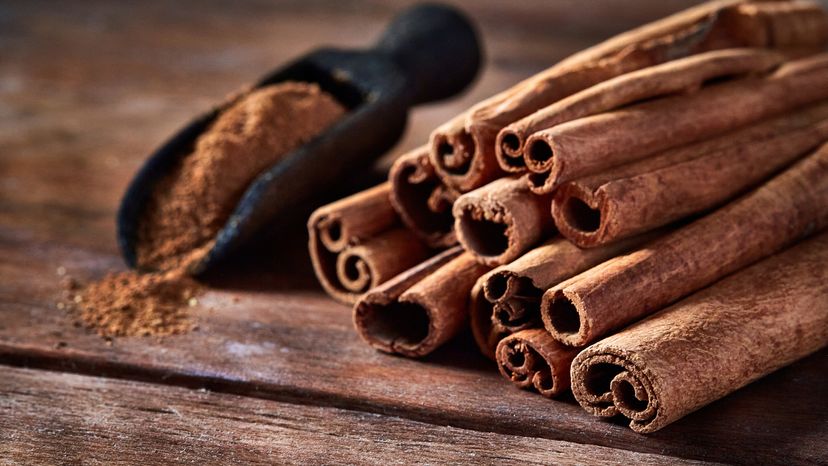 A stack of stick cinnamon and cinnamon powder on a wooden table. 