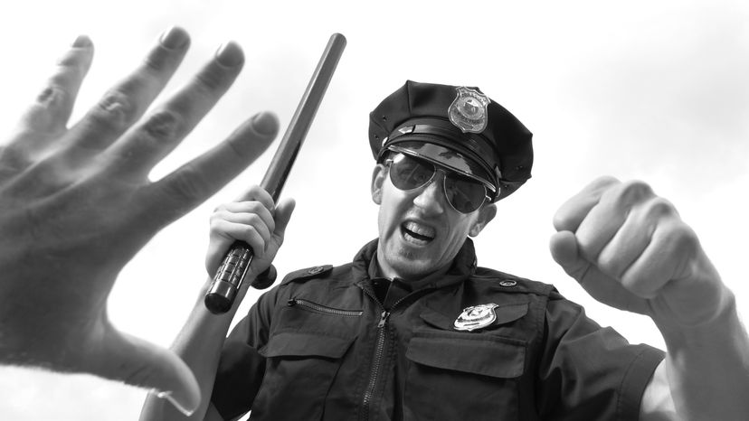 A male police officer threatening a man on the ground. 