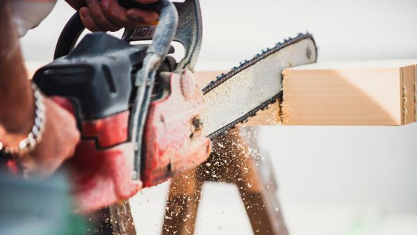 A close up image of a man sawing a wooden beam with a chain saw. 