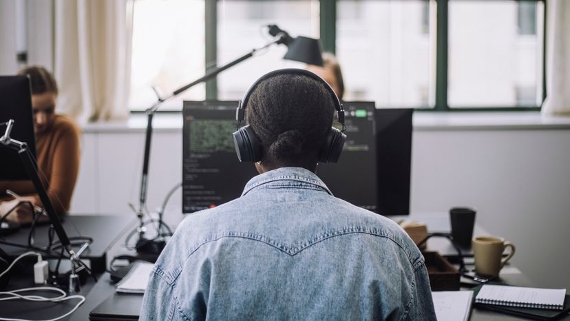 A woman working on her computer while wearing a headset. 