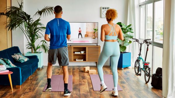 A rear view of young couple working out in the living room while watching an exercise class. 