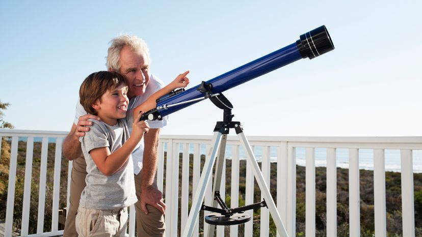 A young boy with his mum looking through a telescope. 