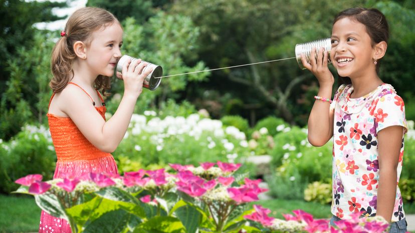 Two young girls talking through two cups on a string. 