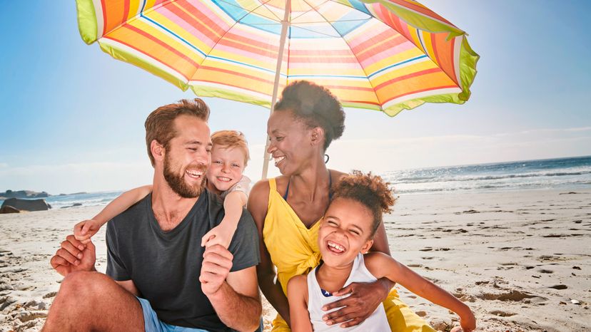 A family of four under an umbrella at the beach. 