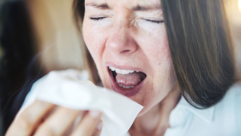 Woman sneezing behind a window, using a tissue.