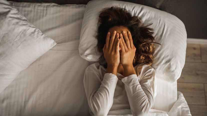 A woman laying in bed with her hands covering her face. 