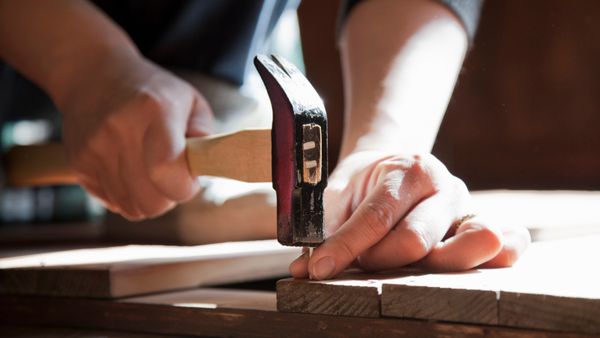 A hand driving a nail into a wood with a hammer.