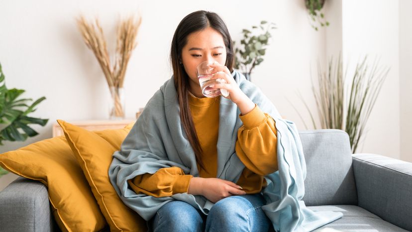 An Asian woman taking pills with a glass of water at home. 