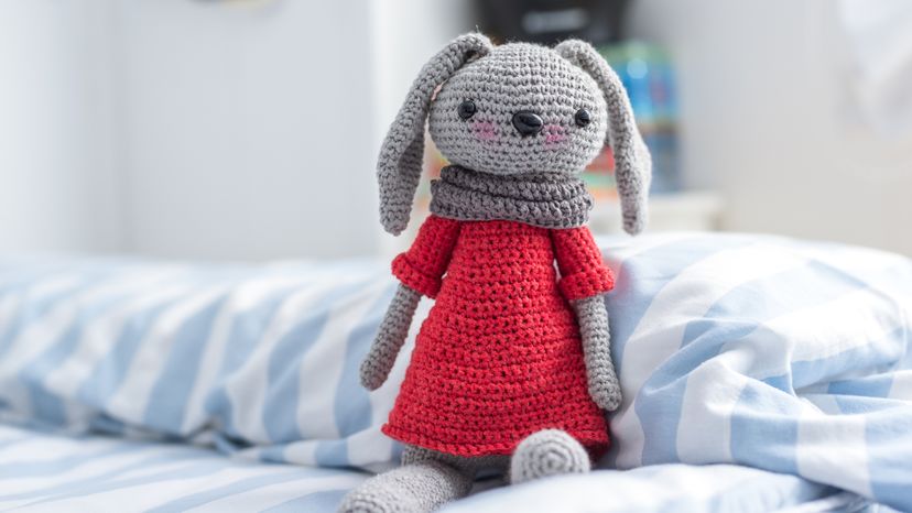 A handmade, knitted doll in red, placed on a bed. 