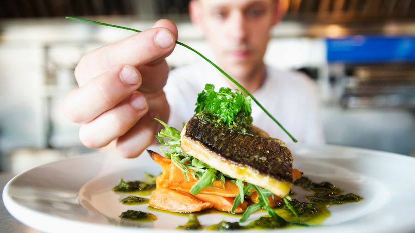 A male chef garnishing a plate of food. 