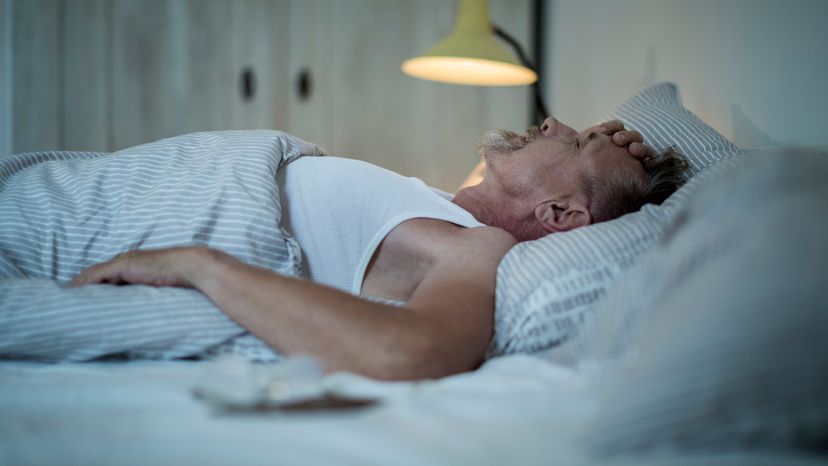 A man laying in bed, with his hand on his head. 