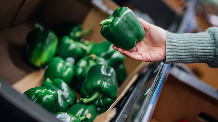 A woman's hand holding up a green pepper in a grocery store. 