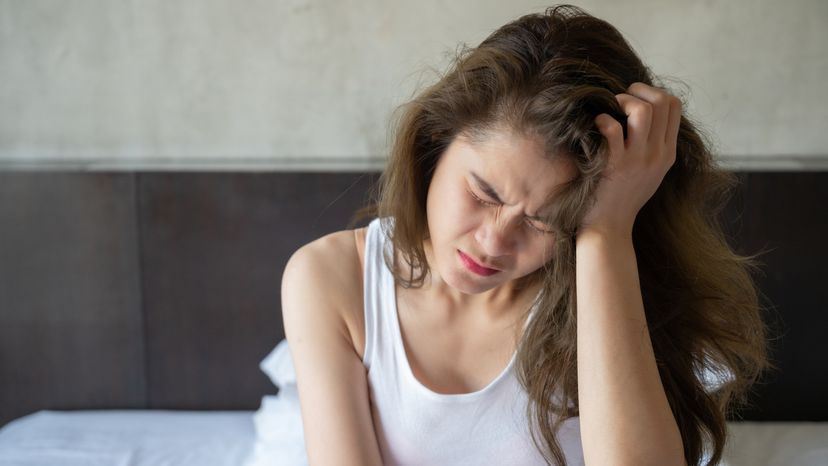 A woman having headache and migraine while sitting on bed.