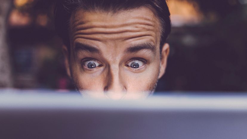 A man with a shocked expression on his face, while watching a movie on his laptop. 