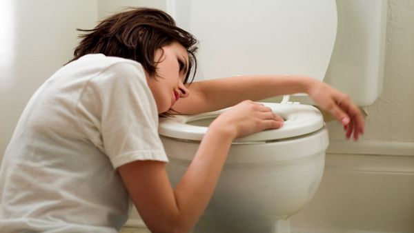 A sick woman sitting on the bathroom floor while laying her head on the toilet seat.