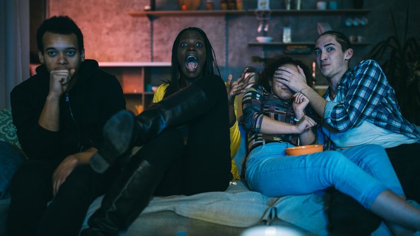 A group of four young friends watching a horror movie at night while eating popcorn. 