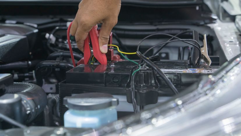 An automotive mechanic using a jump cable to jump start a dead car battery. 