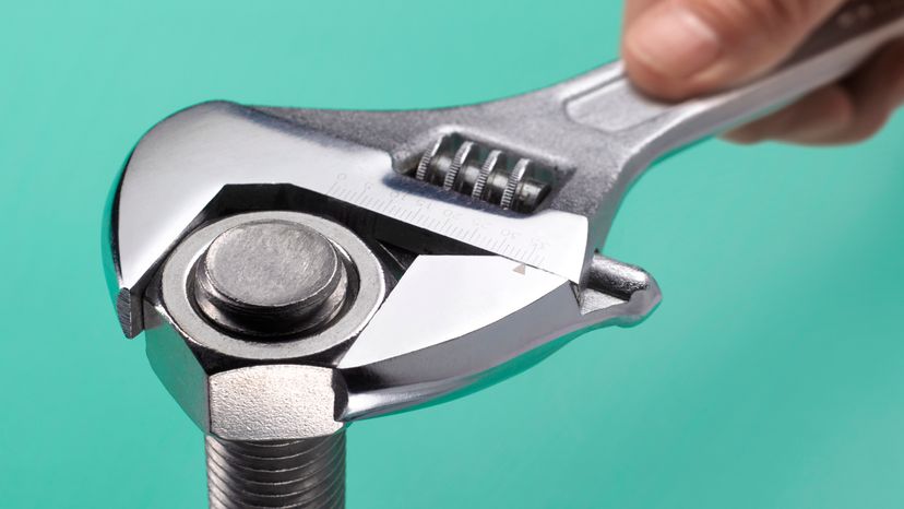 A close up of a hand using an adjustable wrench to tighten a bolt.
