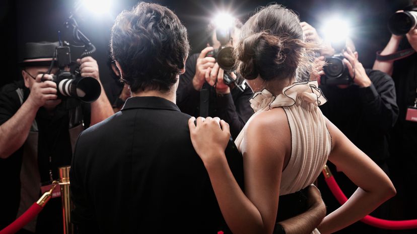 A male and female celebrity standing in front of reporters at a red carpet event.